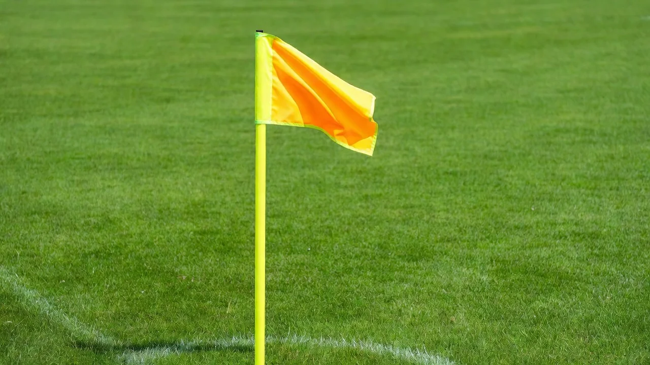 A corner flag with a bright ribbon tied to it waving above green grass