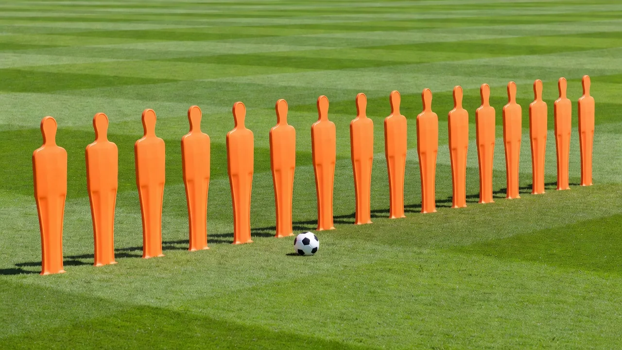 Orange training mannequin row with a ball placed twenty yards away on bright grass