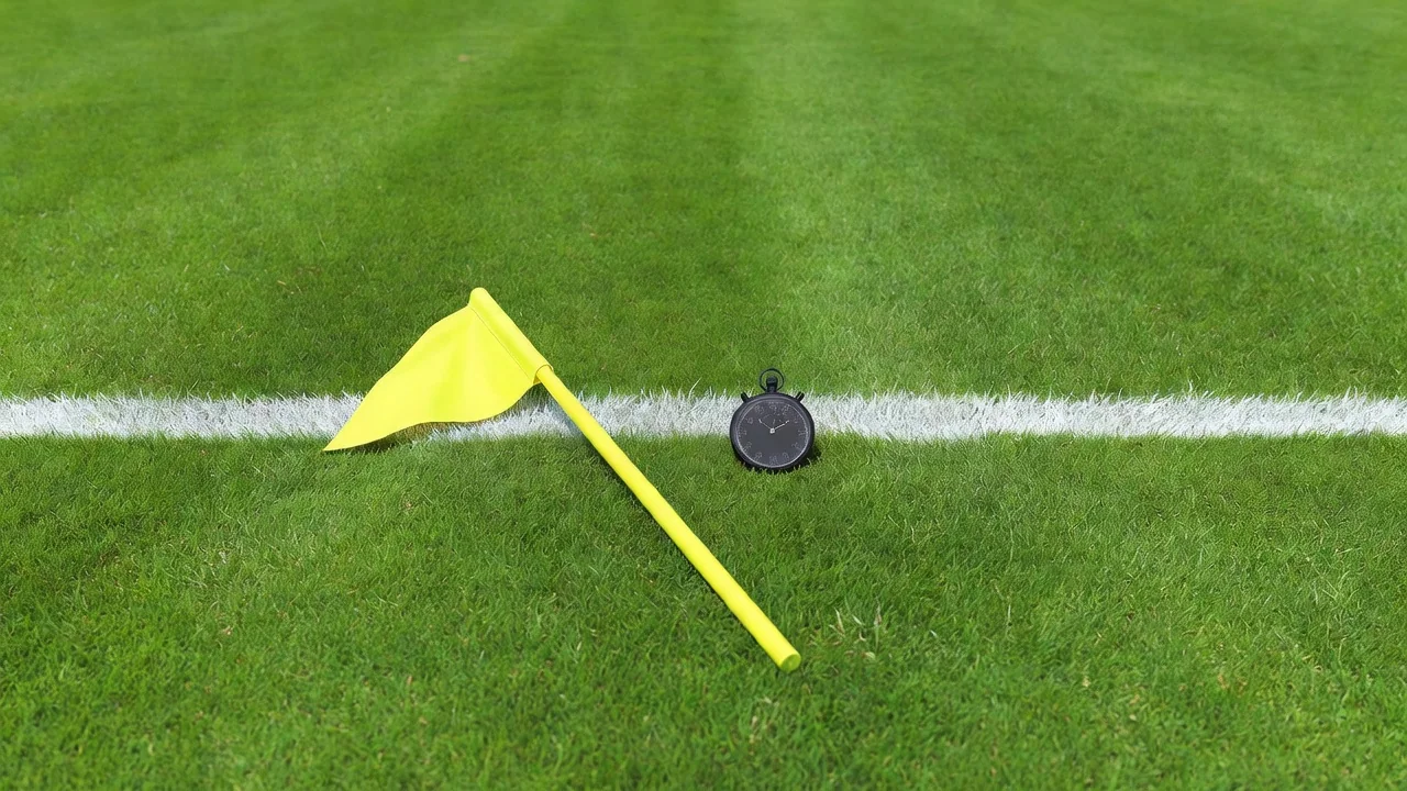 A referee-style flag and a stopwatch on grass beside a touchline