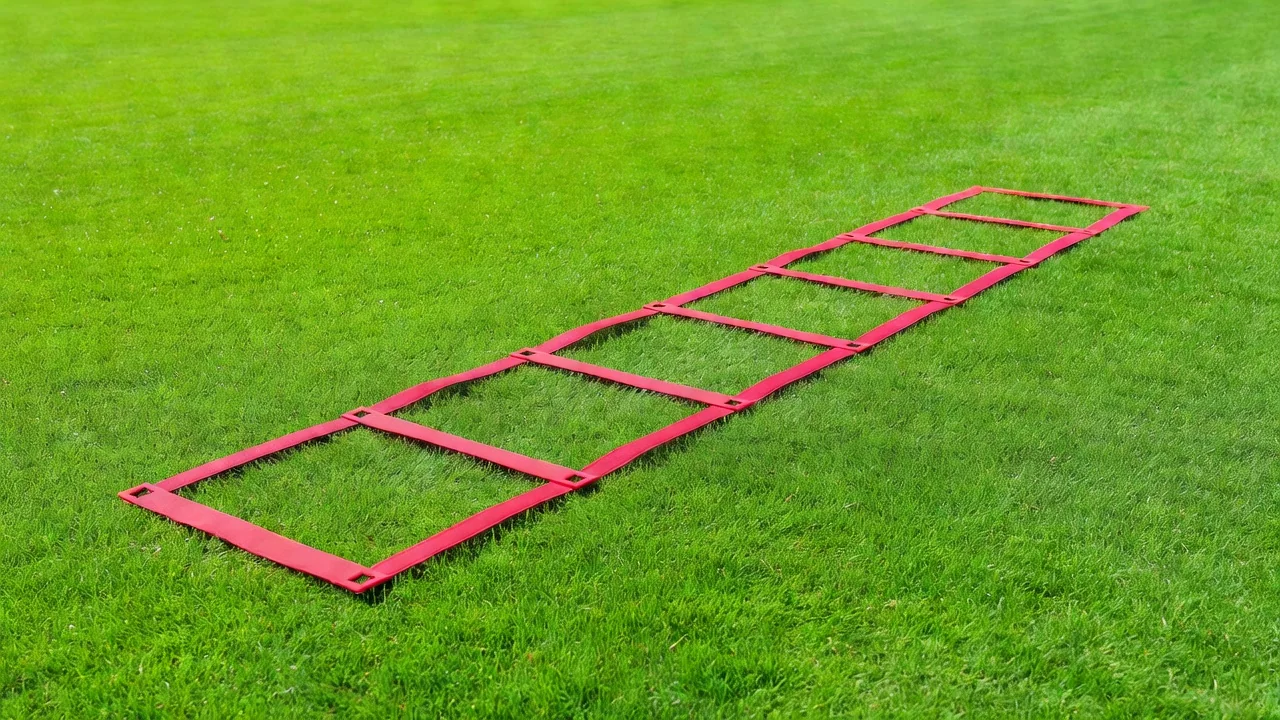 A red training ladder flat on bright grass for footwork drills